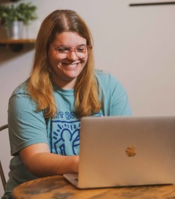 Young woman sitting at table, smiling while looking at a laptop